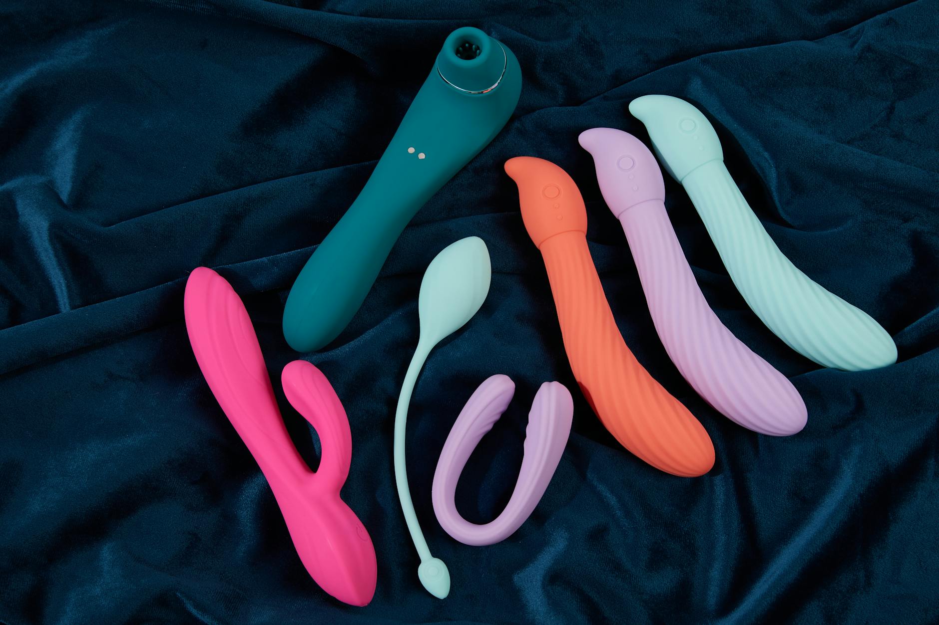 A hand reaching over a variety of colorful sex toys arranged on a table