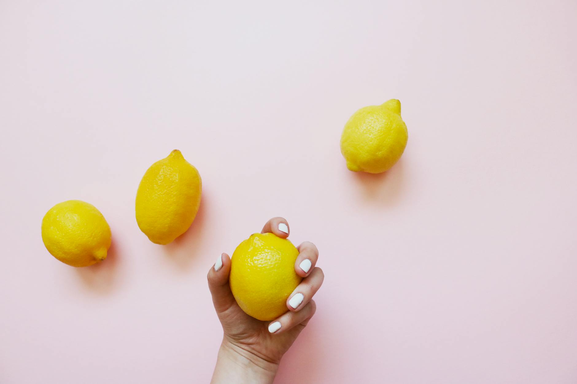 A hand holding a bright lemon on a soft pink background, symbolizing vitality and sensation