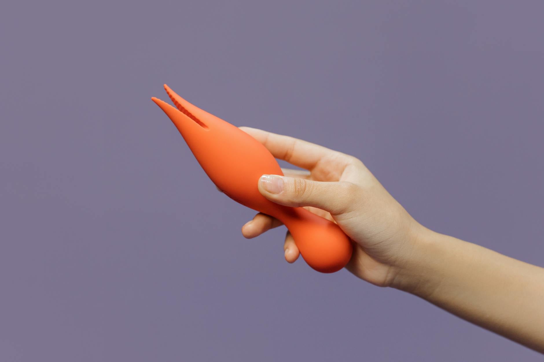 Close-up of a hand holding an orange vibrator against a purple backdrop, showcasing modern sensuality