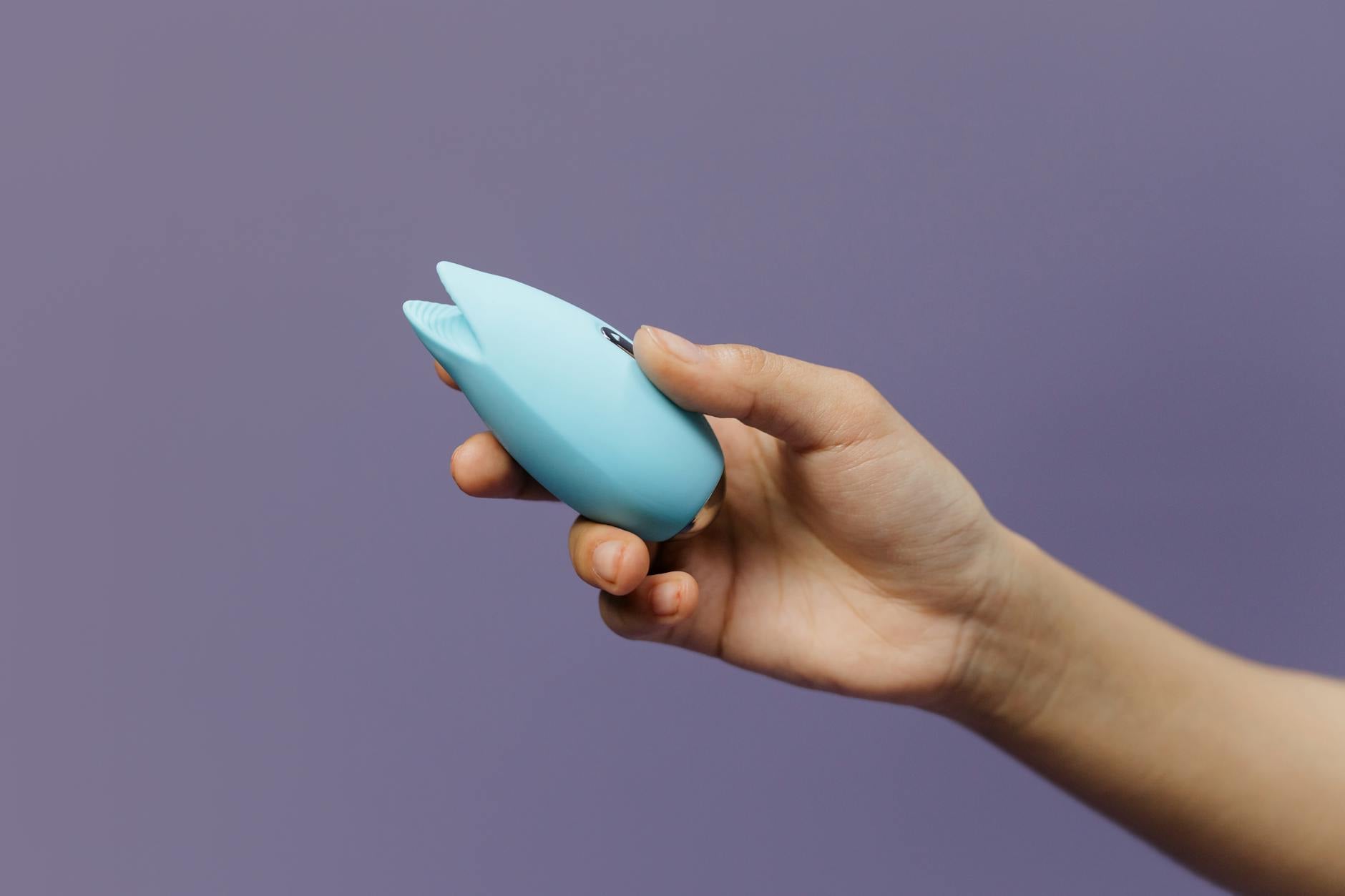 A silicone clitoral vibrator held in hand against a purple background, showing texture and color.